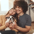 Couple embraces and smiles while holding their pet Bulldog.